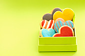 Herzplätzchen mit bunter Zuckerglasur in Schachtel vor grünem Hintergrund