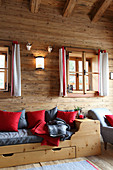 Holzbett mit roten und grauen Kissen in einer Holzhütte