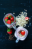 Red strawberry smoothie with chia seeds and oat flakes in jar, served with fresh strawberries over dark background