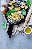 Top view of freshly made raw Italian pasta tortellini, olive oil, flour and basil leaves on light grey vintage background