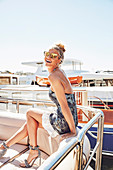 A blonde woman on a yacht wearing a backless dress and sunglasses