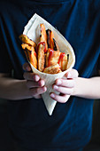 A child holding a mini escalope, sweet potato fries and ketchup in a bamboo cone