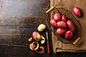 Raw potato in metal basket and burlap bag on wooden background copy space