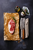 Raw fresh meat steak Striploin with salt and pepper and Butcher Meat cleaver on dark background