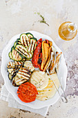 Dish with grilled vegetables, courgettes, aubergines, peppers, tomatoes, spring onions, and scamorza
