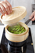 Edamame in a steaming basket on a stove