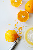 Orangen: Ganz, halbiert, mit Zestenreisser und Saft in Zitruspresse