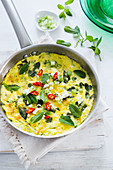A pan with zucchine, spring onions and mint frittata on a white background