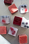 Smoothie ice cubes and ice cubes with berries on a metallic baking sheet