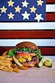 Cheese burger with lettuce tomato, onion, pickle and french fries with american flag