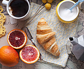 High Angle View of Croissant, Blood Oranges, Cup of Tea and Yellow Sugar Bowl