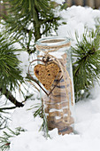 Glas gefüllt mit Plätzchen, dekoriert mit Honigkuchenherz und Herzausstechform im Schnee