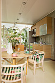Rattan chairs around dining table in front of open-plan kitchen in conservatory