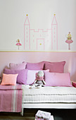 Washi-tape castle on wall above bed with pink scatter cushions