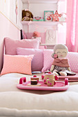 Tablett mit Puppengeschirr und eine Puppe auf dem Bett mit rosa Kissen