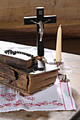 Old books, crucifix, rosary beads, glass and candle on wooden table