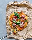 A spaghetti pizza with tomatoes, ham and rocket