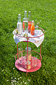 Bottles of soft drinks and delicate cherry blossom on round side table in garden