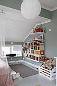 Puppenhaus, Regale und Kiste mit Spielzeug im Mädchenzimmer mit grauer Wand und Dachschräge
