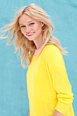Junge, blonde Frau in gelbem Pulli vor blauem Hintergrund
