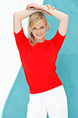 A young blonde woman wearing a red, short-sleeved jumper against a blue background