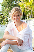 A young blonde woman wearing a white summer jumper by the sea