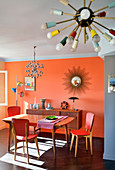 Dining area and sideboard in retro interior with orange wall