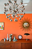 Sideboard below sunburst mirror on orange wall