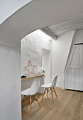 Shell chairs at narrow desk below skylight