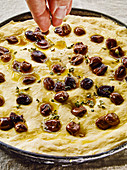 Olive focaccia being sprinkled with oregano