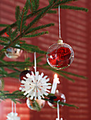 Rote Rose in einer Christbaumkugel aus Glas und Papierornament
