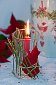 Glas mit Weihnachtsstern und Kiefernnadeln dekoriert, als Windlicht