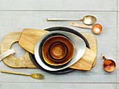 Various bowls and boards next to cutlery, a copper jug and a copper spoon