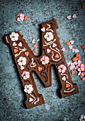 A chocolate letter M decorated with sugar flowers and hearts