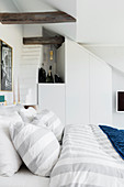 Weißes Schlafzimmer mit Doppelbett, darüber rustikale Holzbalken