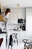 Woman standing on counter in pale grey fitted kitchen with marble splashback