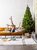 Blond woman lying on ocher sofa in front of Christmas tree