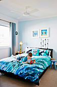 Boy with book lies on bed of blue bedding