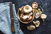 Various fresh mushrooms in a wooden bowl and next to it