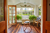 Rattan furniture, a chest and green plants in the winter garden with a rustic wooden floor