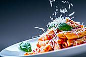 Cheese being sprinkled on penne with tomato sauce and basil