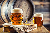 Bier mit Schaum im Bierkrug, im Hintergrund Holzfaß