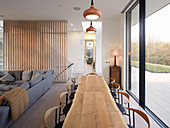 Long wooden table in open-plan interior next to glass wall overlooking terrace