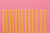Spaghetti aufgereiht vor rosafarbenem Hintergrund