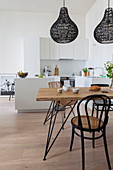 Dining table and various chairs below black pendant lamps in open-plan kitchen