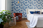 Blue-and-white, leaf-patterned wallpaper and designer furniture in bedroom