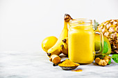 Yellow fruit smoothie with turmeric and ingredients on a table