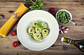 Spaghetti mit Basilikumpesto, Tomaten und Olivenöl, umgeben von Zutaten