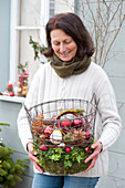Frau bringt Drahtkorb mit Christbaumkugeln, Zapfen und Moos