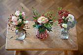Drei kleine Blumensträuße in Vasen auf einem alten Holzschemel